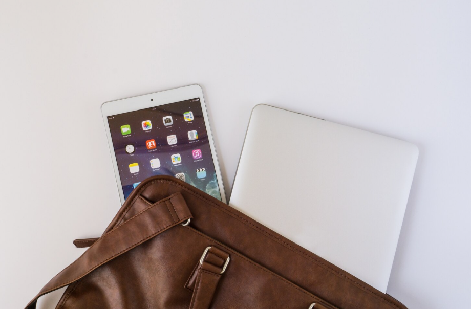 Tablet and laptop tucked in a brown leather bag, representing a minimal tech setup for a digital declutter.