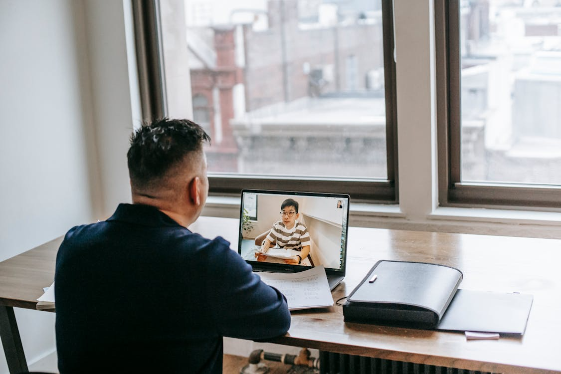 Man attending an online learning session via video call on a laptop in a modern office setting