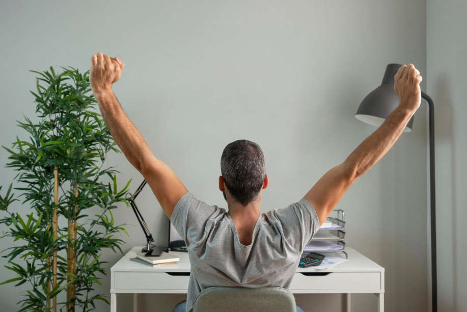 Man stretching at his desk with raised arms after completing a short micro workout