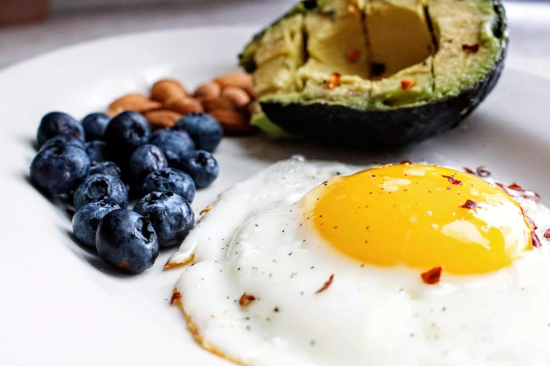 Plate with fried egg, avocado, and blueberries illustrating a mindful eating breakfast.