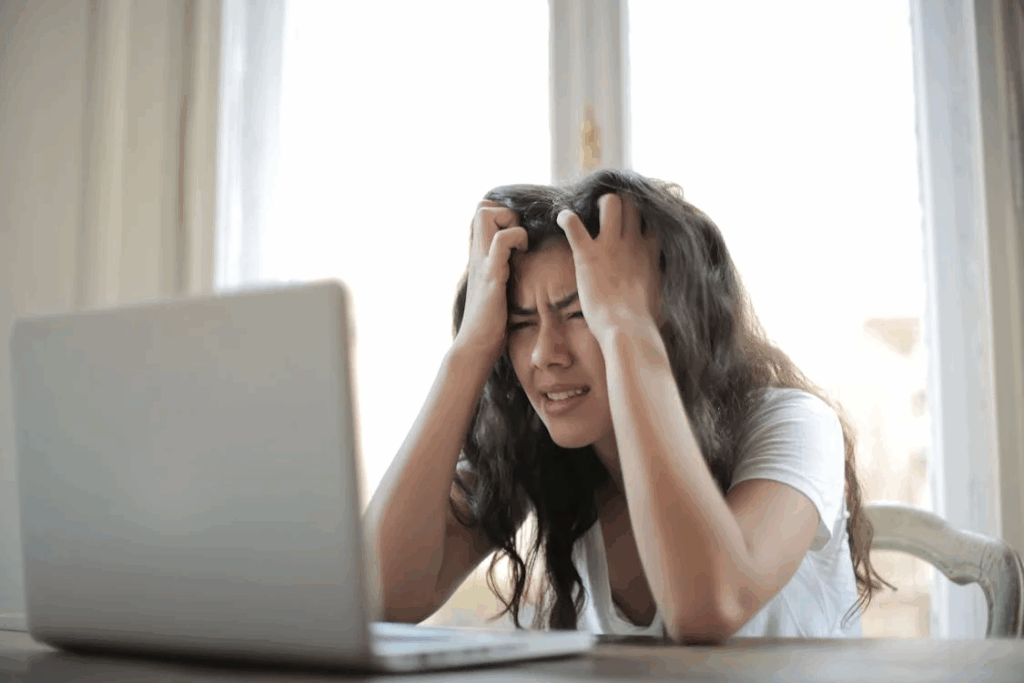Stressed woman holding her head while working on a laptop, showing signs of burnout.