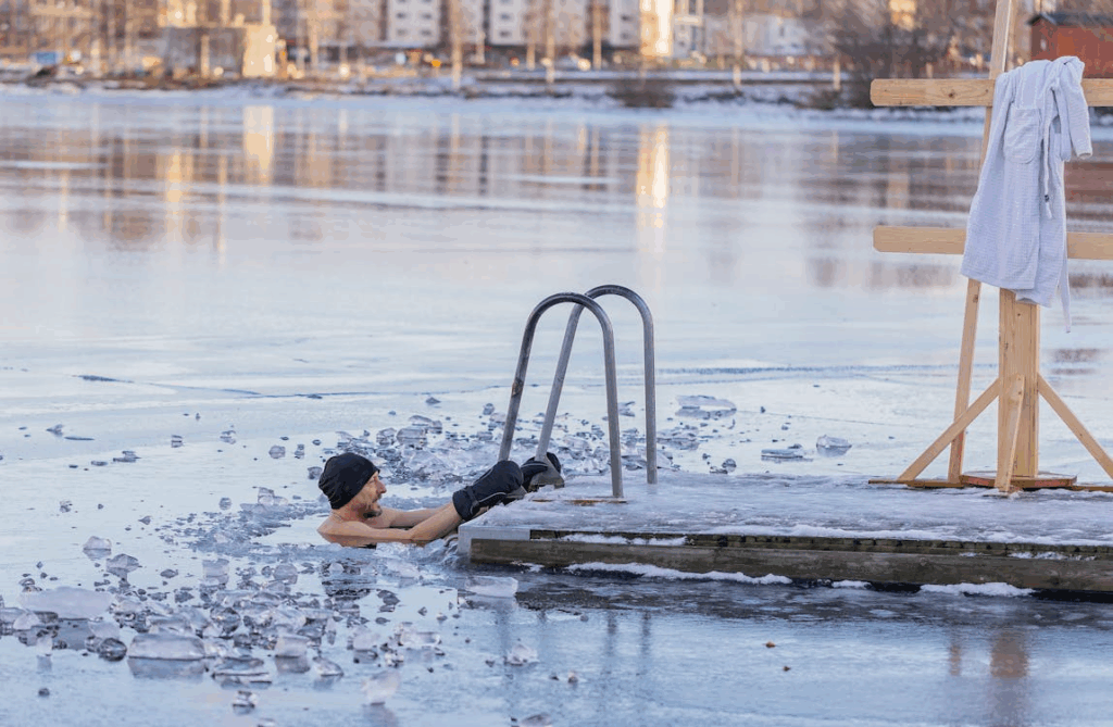Man doing a cold plunge in a frozen lake beside a dock ladder