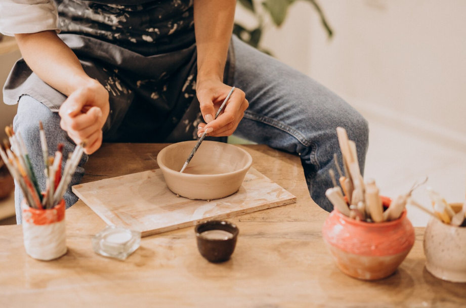 Person glazing a handmade clay bowl, symbolizing learning new skills to reinvent yourself.