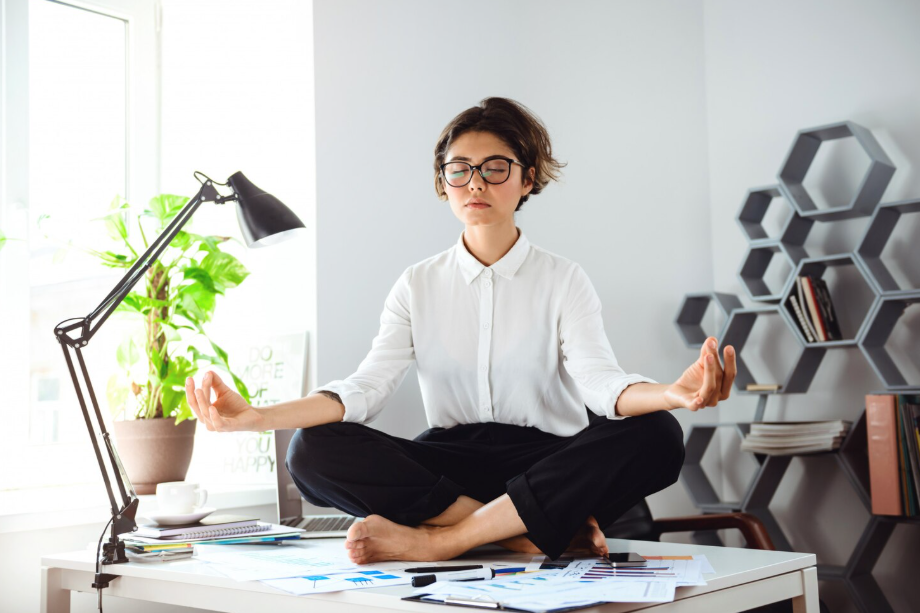 Woman meditating in the office, practicing stress management techniques.