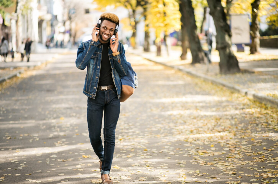 Smiling man in headphones walking along a tree-lined city path, practicing walking meditation