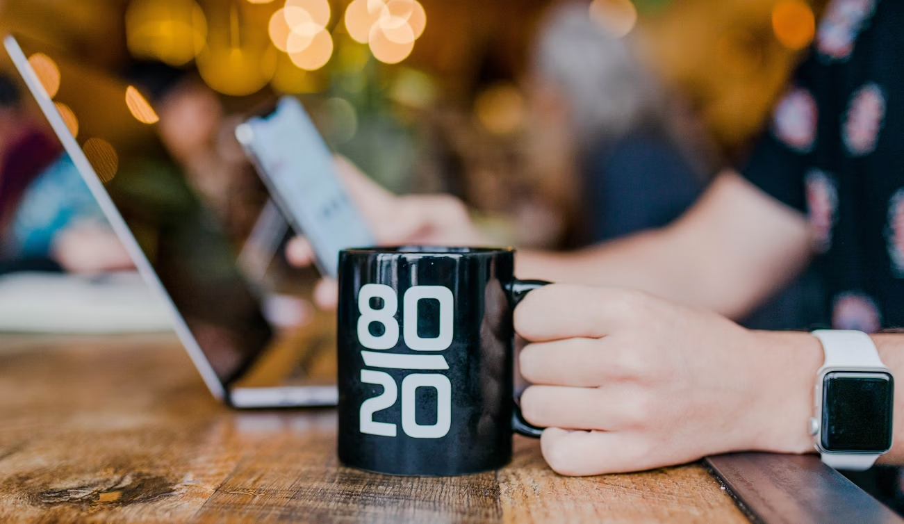 Person holding a black coffee mug with “80/20” text, representing the 80/20 Rule
